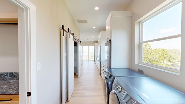 washroom featuring a barn door, light hardwood / wood-style floors, plenty of natural light, and washer and clothes dryer