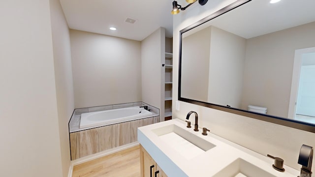 bathroom featuring tiled tub, hardwood / wood-style floors, vanity, and toilet