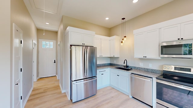 kitchen featuring sink, appliances with stainless steel finishes, decorative light fixtures, light hardwood / wood-style floors, and white cabinetry