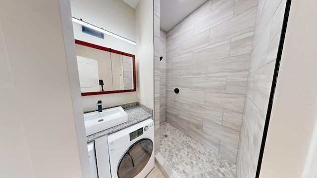 bathroom featuring vanity, a tile shower, and washer / clothes dryer