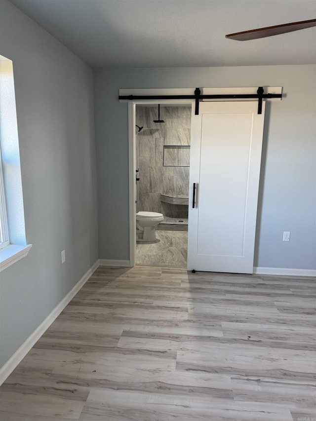 unfurnished bedroom featuring a barn door, light hardwood / wood-style floors, and connected bathroom