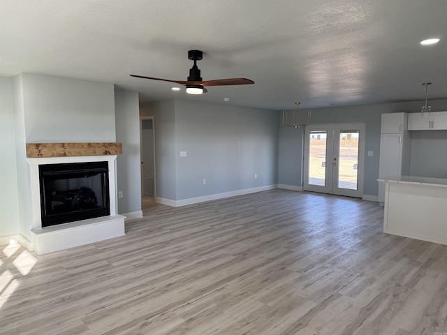 unfurnished living room featuring a textured ceiling, ceiling fan, light hardwood / wood-style flooring, and french doors