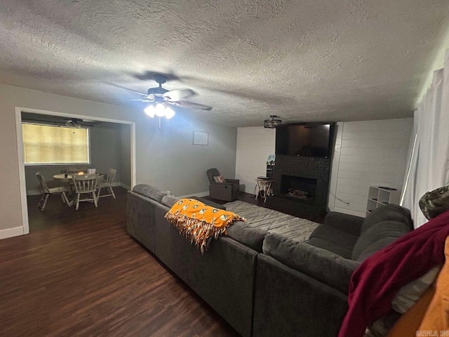 living room featuring a textured ceiling, ceiling fan, a large fireplace, and dark wood-type flooring