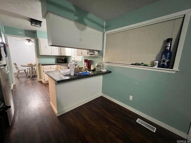 kitchen with kitchen peninsula, dark hardwood / wood-style flooring, white cabinets, and a textured ceiling