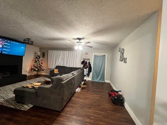 living room with a textured ceiling, ceiling fan, a fireplace, and dark wood-type flooring