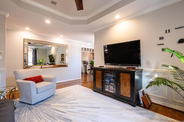 living room with a tray ceiling, ceiling fan, ornamental molding, and wood-type flooring