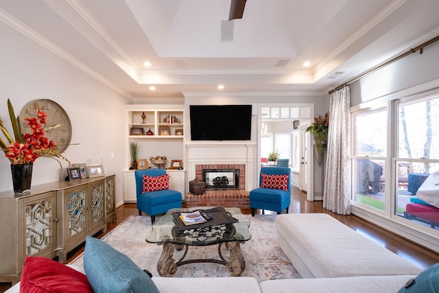 living room with a fireplace, ornamental molding, a tray ceiling, and dark hardwood / wood-style flooring