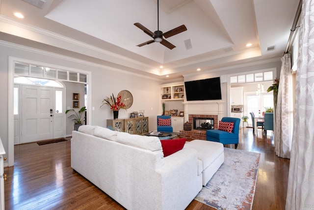 living room with a brick fireplace, crown molding, dark wood-type flooring, and a tray ceiling