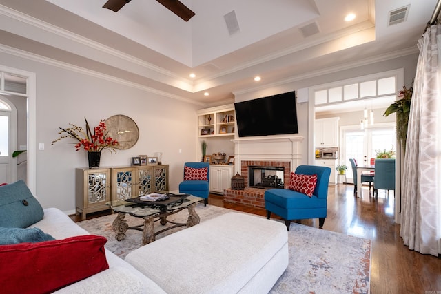 living room featuring crown molding, hardwood / wood-style floors, a brick fireplace, and a raised ceiling