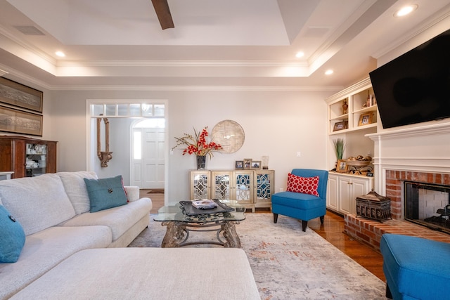 living room featuring a fireplace, dark wood-type flooring, a tray ceiling, and crown molding