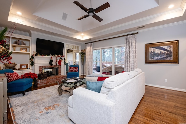 living room featuring ceiling fan, hardwood / wood-style floors, a brick fireplace, and a tray ceiling