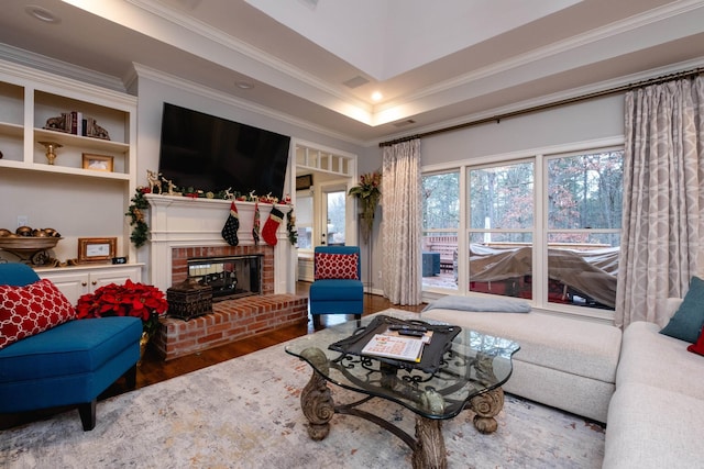 living room with hardwood / wood-style flooring, a raised ceiling, crown molding, and a fireplace