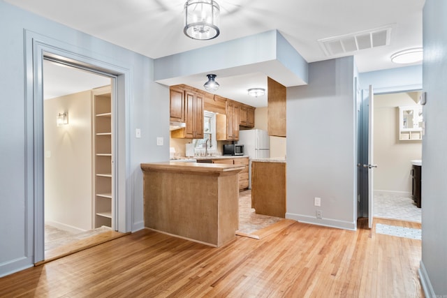 kitchen with kitchen peninsula, extractor fan, sink, an inviting chandelier, and light hardwood / wood-style floors