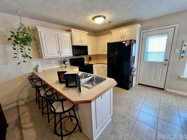 kitchen featuring a kitchen breakfast bar, kitchen peninsula, white cabinetry, and black appliances