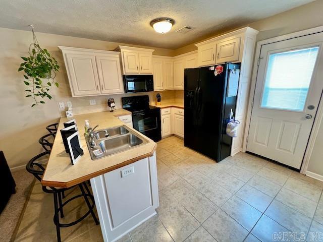 kitchen featuring a breakfast bar, black appliances, sink, a textured ceiling, and white cabinetry