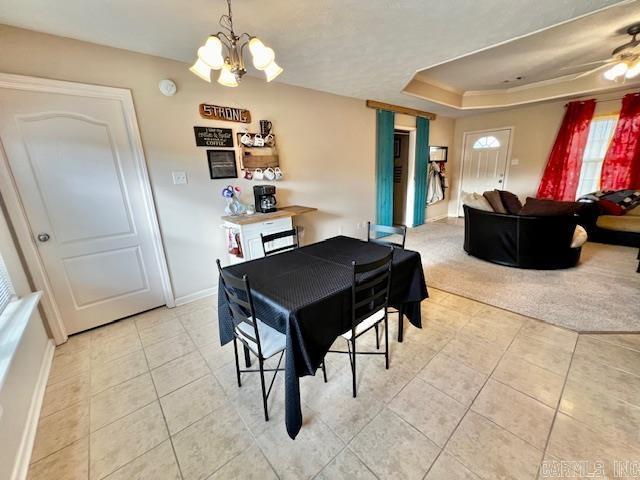 tiled dining room featuring ceiling fan with notable chandelier and a raised ceiling