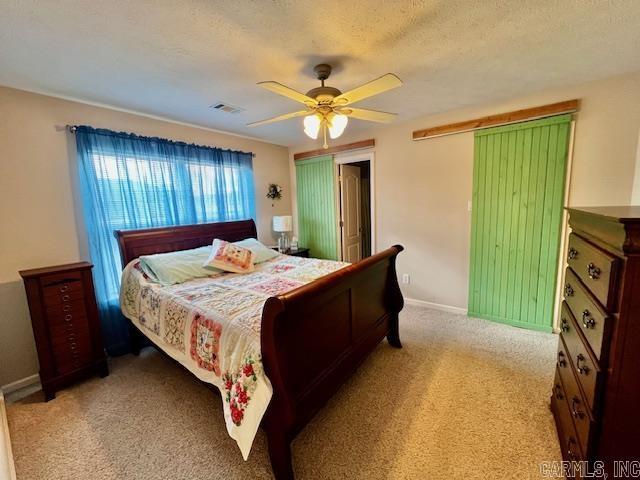 bedroom with ceiling fan, light colored carpet, and a textured ceiling