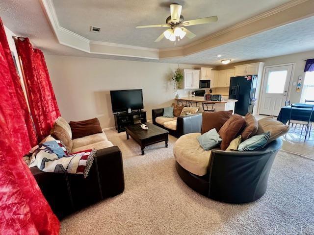 living room with light colored carpet, ceiling fan, a raised ceiling, and ornamental molding