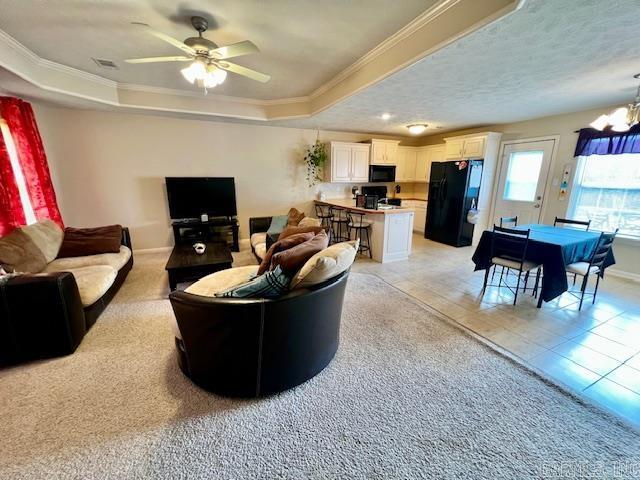 living room with light carpet, ceiling fan with notable chandelier, a tray ceiling, and crown molding