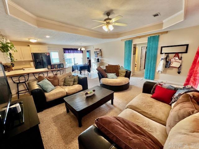 living room featuring a raised ceiling, ceiling fan with notable chandelier, and ornamental molding