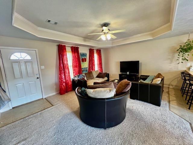 carpeted living room featuring ceiling fan, a raised ceiling, and ornamental molding