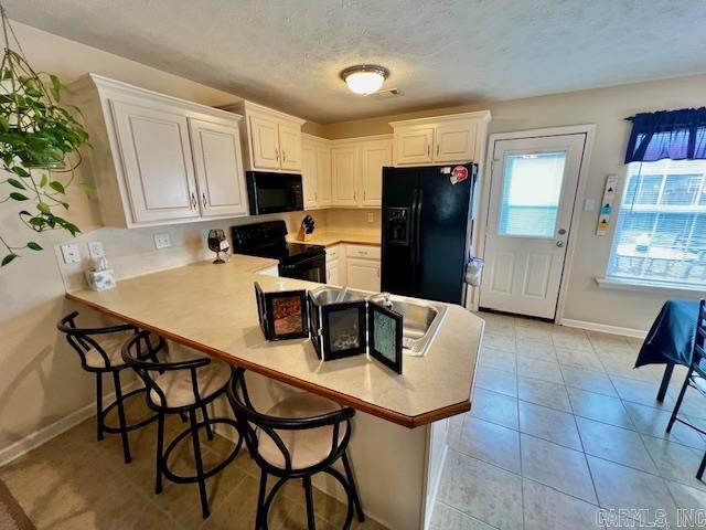 kitchen with kitchen peninsula, a textured ceiling, black appliances, white cabinets, and a breakfast bar area