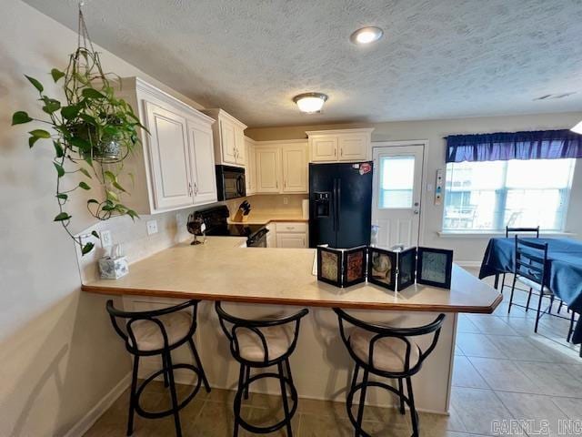 kitchen with kitchen peninsula, a kitchen bar, white cabinets, and black appliances