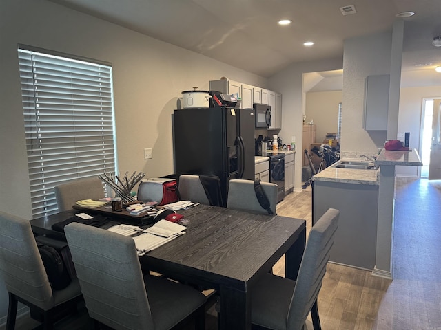 dining space with sink, vaulted ceiling, and light hardwood / wood-style floors