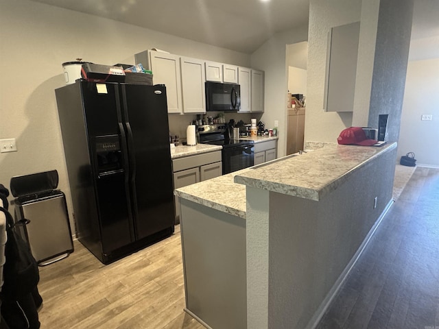 kitchen featuring vaulted ceiling, kitchen peninsula, light wood-type flooring, and black appliances