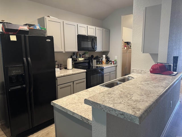 kitchen with lofted ceiling, sink, black appliances, kitchen peninsula, and light wood-type flooring