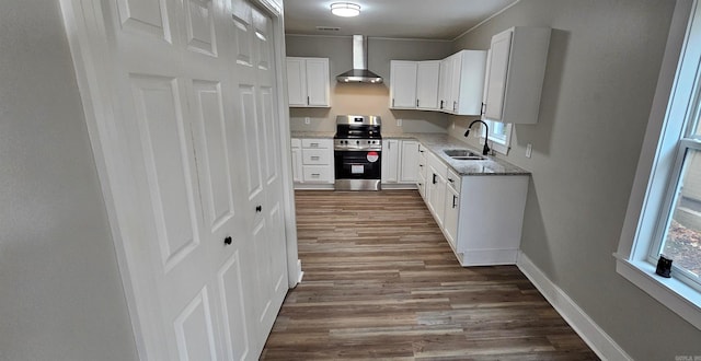 kitchen with white cabinetry, stainless steel range oven, sink, and wall chimney range hood