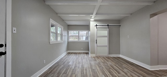 unfurnished bedroom with beam ceiling, a barn door, hardwood / wood-style flooring, and coffered ceiling