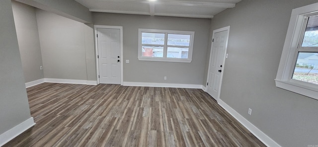 spare room with plenty of natural light, beam ceiling, and dark wood-type flooring