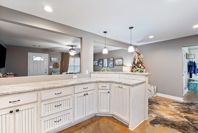 kitchen with kitchen peninsula, light stone countertops, white cabinets, and concrete flooring