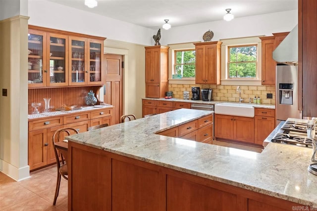 kitchen featuring sink, light stone counters, stainless steel refrigerator with ice dispenser, a breakfast bar area, and decorative backsplash