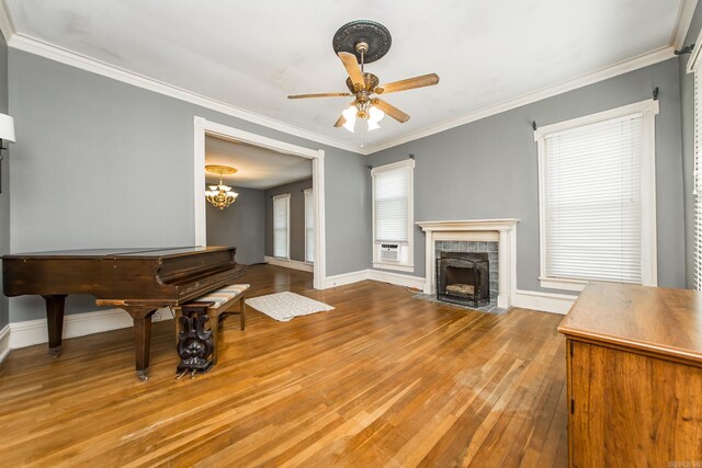 miscellaneous room with ceiling fan with notable chandelier, ornamental molding, light hardwood / wood-style flooring, and a tiled fireplace