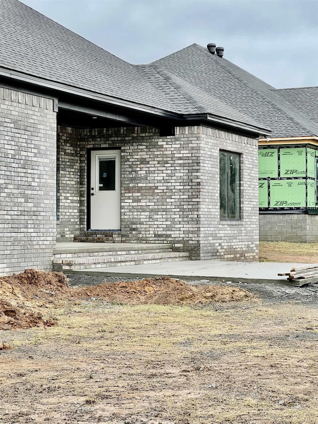 view of property exterior featuring brick siding and roof with shingles