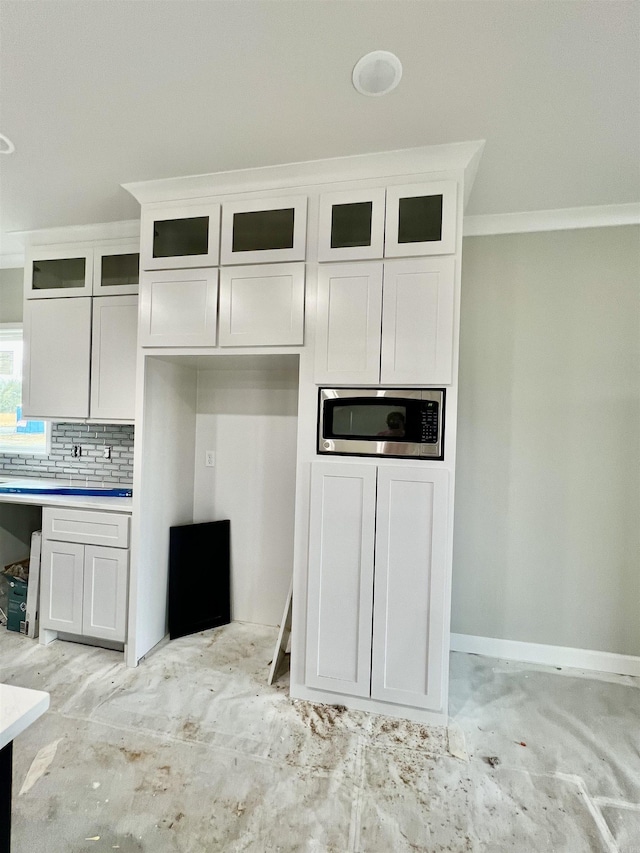 kitchen featuring white cabinets, backsplash, stainless steel microwave, and ornamental molding