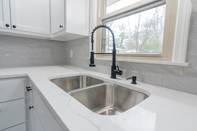 interior details featuring light stone countertops, sink, and white cabinets