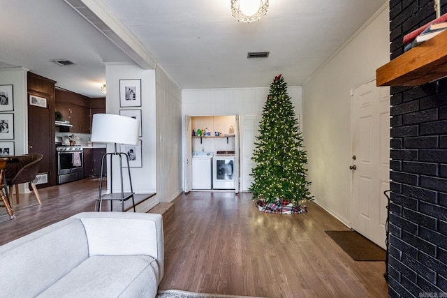 living room featuring independent washer and dryer, crown molding, and dark wood-type flooring