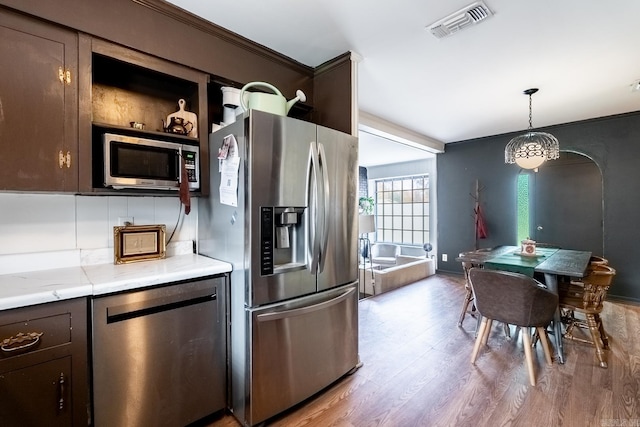 kitchen featuring decorative backsplash, dark brown cabinetry, stainless steel appliances, and hanging light fixtures