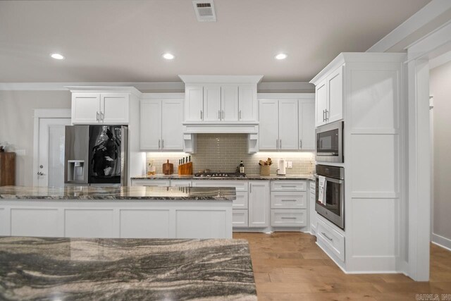 kitchen with light wood-type flooring, white cabinetry, stainless steel appliances, and dark stone counters