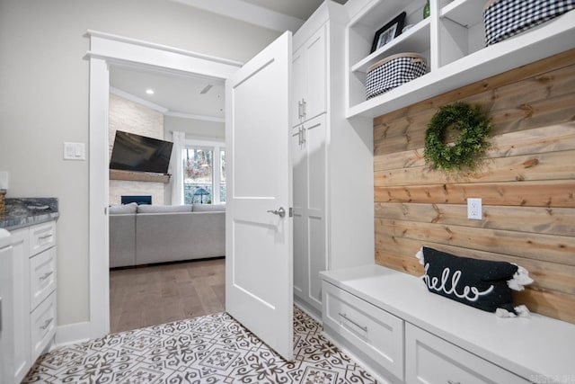 mudroom with a stone fireplace, crown molding, and light wood-type flooring