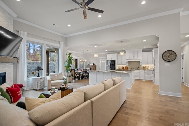 living room featuring light hardwood / wood-style floors, a stone fireplace, ceiling fan, and ornamental molding