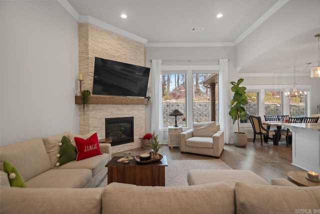living room with a fireplace, an inviting chandelier, light hardwood / wood-style flooring, and ornamental molding