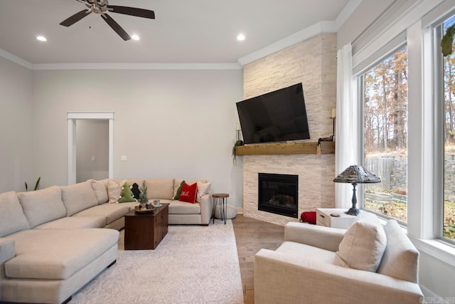living room featuring light hardwood / wood-style flooring, ceiling fan, crown molding, and a stone fireplace