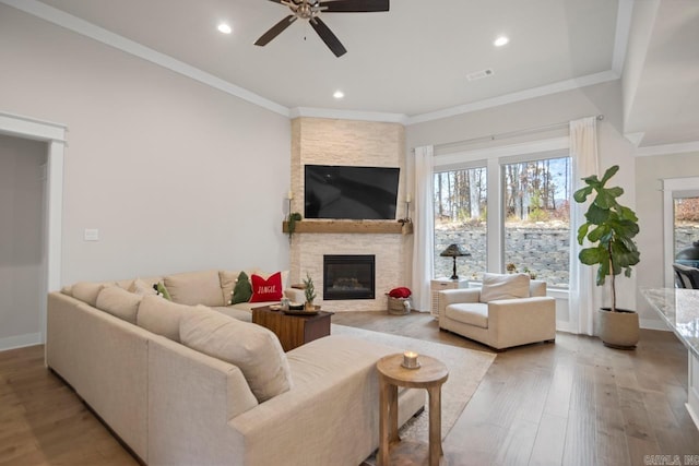 living room featuring ceiling fan, a stone fireplace, crown molding, and light hardwood / wood-style flooring