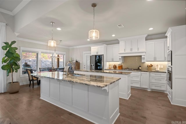 kitchen featuring stainless steel appliances, a kitchen island with sink, sink, white cabinetry, and hanging light fixtures