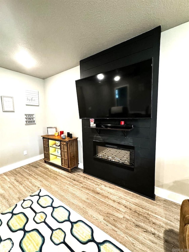 recreation room featuring a large fireplace, wood-type flooring, and a textured ceiling