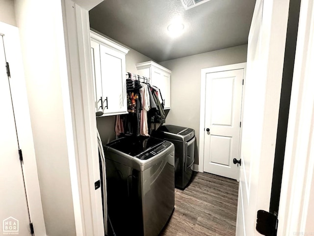 laundry room with cabinets, wood-type flooring, a textured ceiling, and washer and clothes dryer